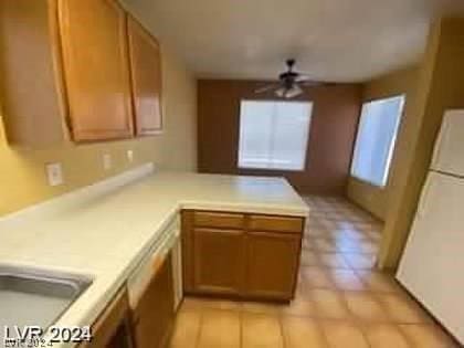 kitchen with light countertops, brown cabinets, a peninsula, freestanding refrigerator, and a ceiling fan