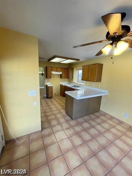 kitchen featuring brown cabinetry, a peninsula, a sink, light countertops, and under cabinet range hood