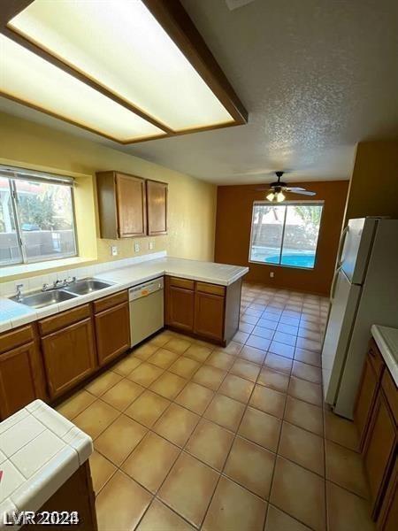 kitchen with a sink, brown cabinets, freestanding refrigerator, and stainless steel dishwasher