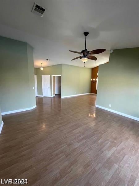 spare room with dark wood-type flooring, a ceiling fan, visible vents, and baseboards