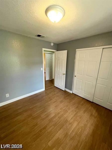 unfurnished bedroom with wood finished floors, visible vents, baseboards, a closet, and a textured ceiling