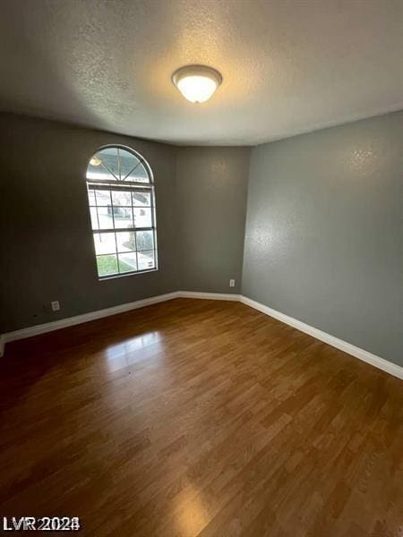 spare room featuring baseboards, a textured ceiling, and dark wood finished floors