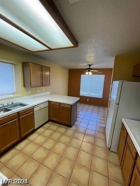 kitchen featuring dishwasher, light countertops, a peninsula, freestanding refrigerator, and brown cabinetry