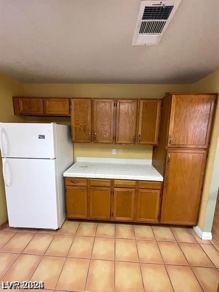 kitchen featuring light tile patterned floors, visible vents, brown cabinetry, and freestanding refrigerator