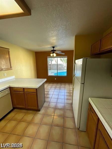 kitchen featuring brown cabinets, light tile patterned flooring, white appliances, a textured ceiling, and a ceiling fan