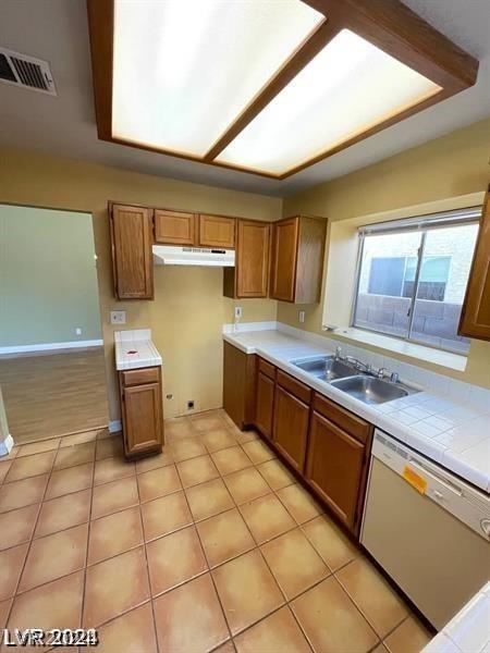 kitchen featuring under cabinet range hood, brown cabinets, dishwasher, and a sink