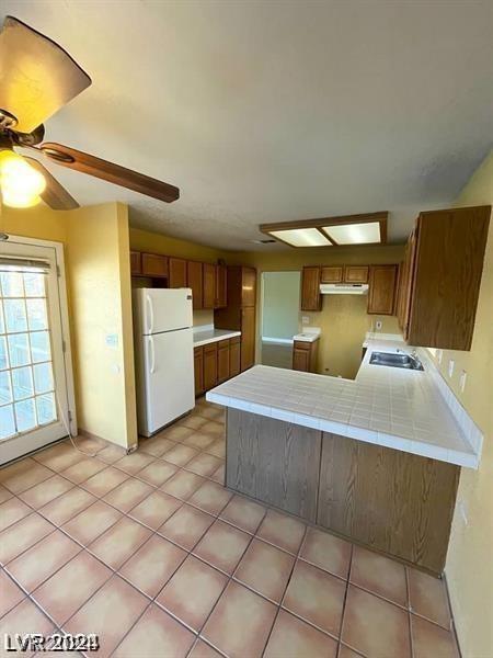 kitchen with under cabinet range hood, brown cabinets, a peninsula, freestanding refrigerator, and a sink