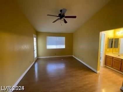 interior space with light wood-style flooring, ensuite bath, baseboards, and vaulted ceiling