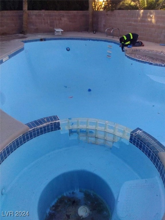 view of pool with a diving board, a pool with connected hot tub, and fence