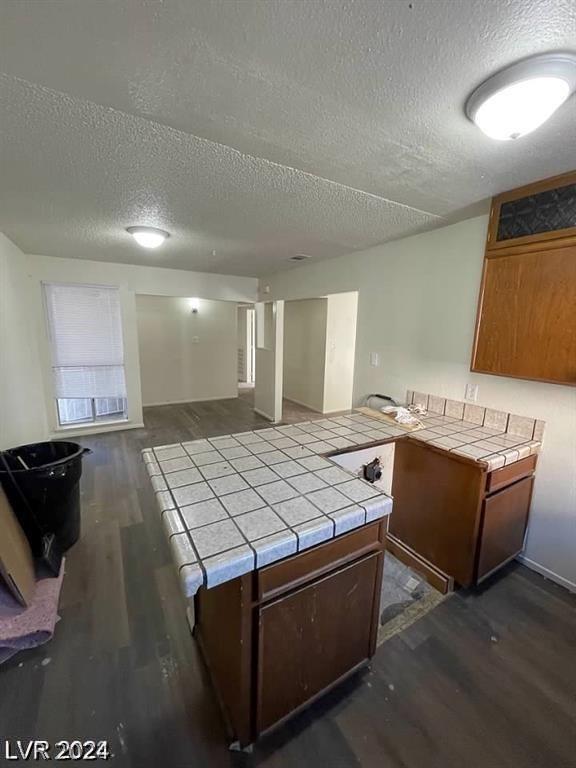 kitchen with dark wood-type flooring, tile counters, and a textured ceiling