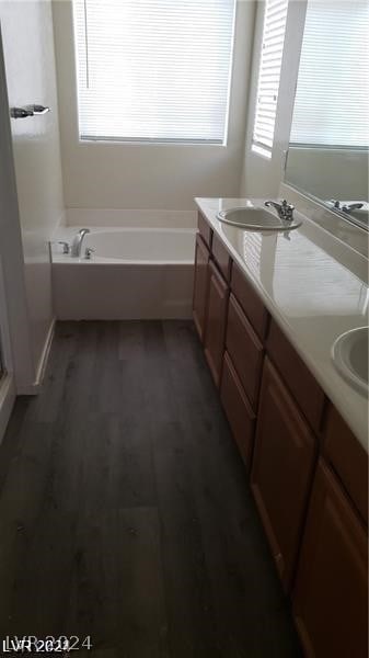 bathroom featuring a healthy amount of sunlight, wood-type flooring, dual bowl vanity, and a tub