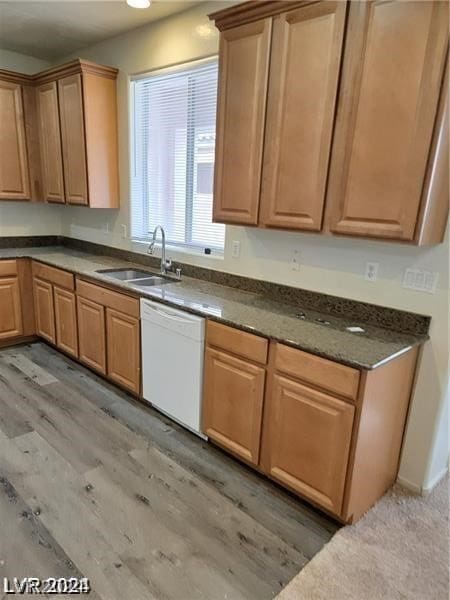 kitchen with dark stone countertops, white dishwasher, sink, and light wood-type flooring