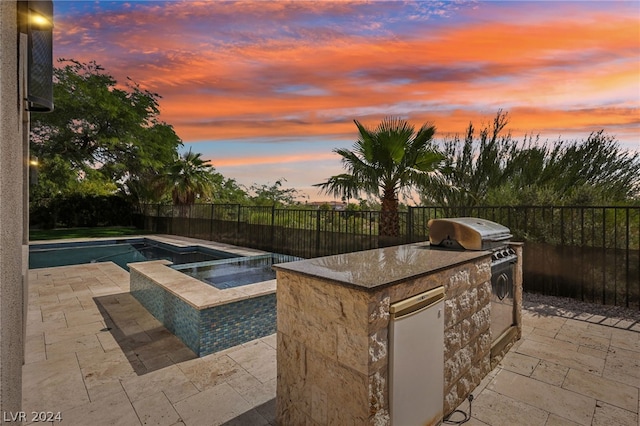 pool at dusk with a patio area, an outdoor kitchen, and an in ground hot tub