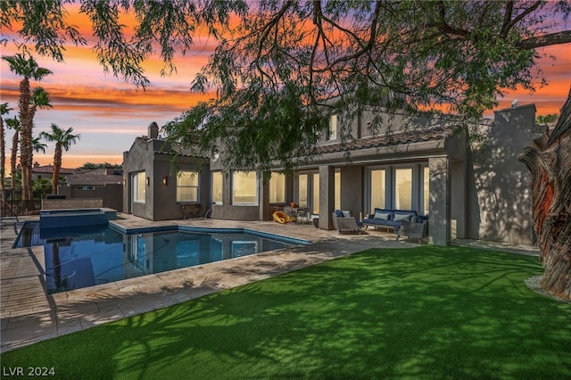 back house at dusk featuring a yard and a patio