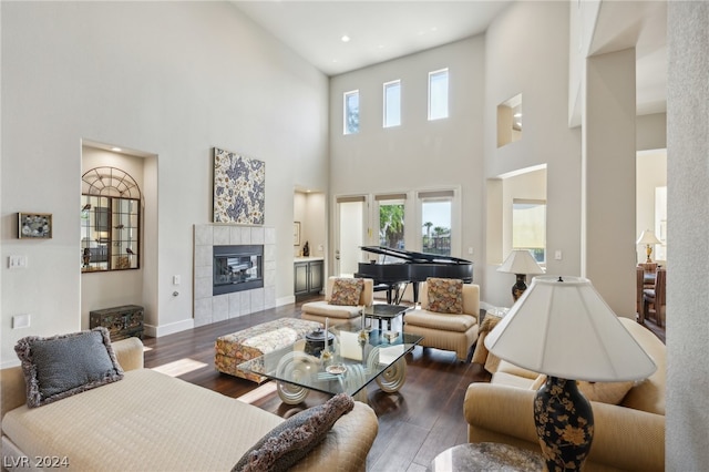 living room with a towering ceiling, dark wood-type flooring, a healthy amount of sunlight, and a tile fireplace