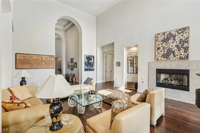 living room with dark hardwood / wood-style flooring, a tiled fireplace, and a high ceiling