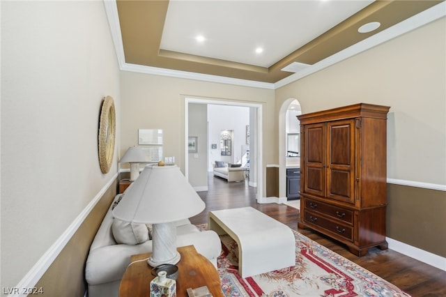 living area featuring dark wood-type flooring, a raised ceiling, and ornamental molding