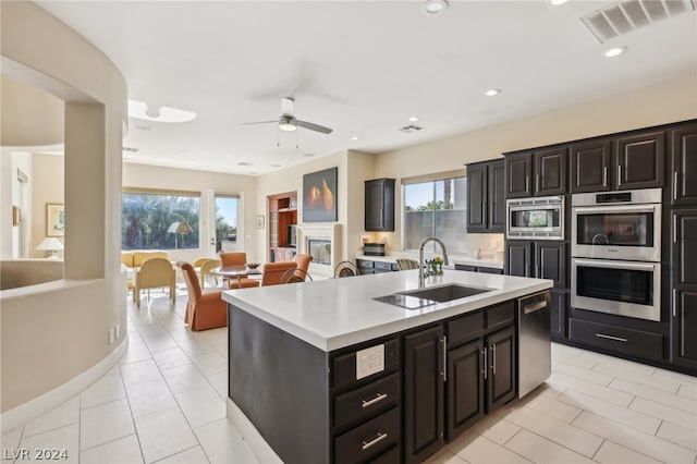 kitchen with sink, appliances with stainless steel finishes, ceiling fan, light tile patterned floors, and an island with sink