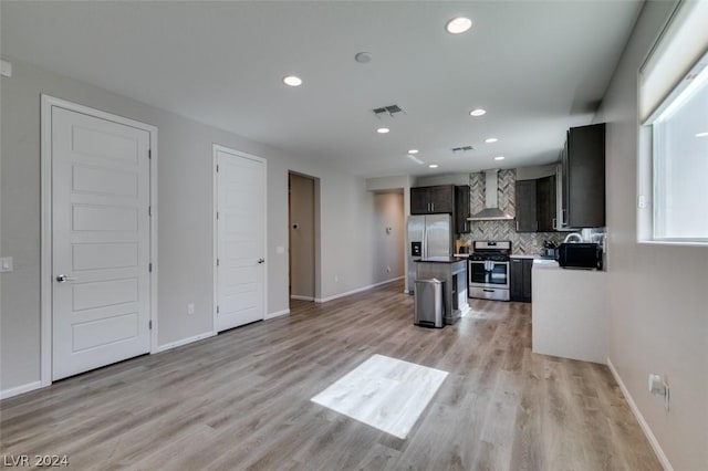 kitchen with wall chimney exhaust hood, a center island, light hardwood / wood-style flooring, stainless steel appliances, and decorative backsplash