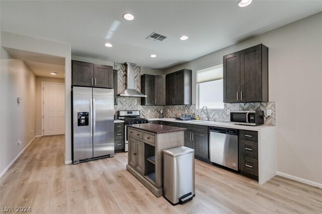 kitchen with tasteful backsplash, wall chimney exhaust hood, a center island, appliances with stainless steel finishes, and light hardwood / wood-style flooring