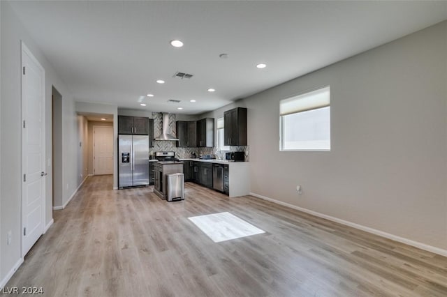 kitchen with wall chimney range hood, backsplash, light hardwood / wood-style flooring, and stainless steel appliances