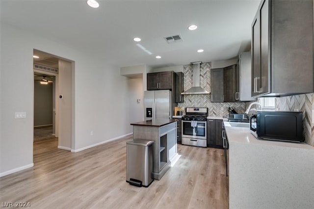 kitchen featuring sink, appliances with stainless steel finishes, tasteful backsplash, a kitchen island, and wall chimney exhaust hood