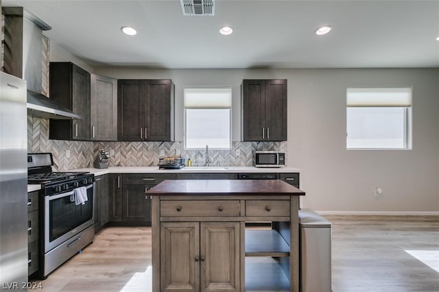 kitchen with sink, appliances with stainless steel finishes, dark brown cabinetry, tasteful backsplash, and light hardwood / wood-style floors