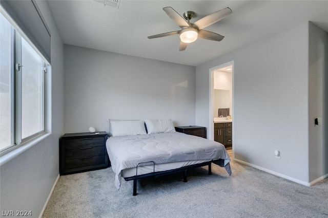 bedroom with ensuite bathroom, light colored carpet, and ceiling fan