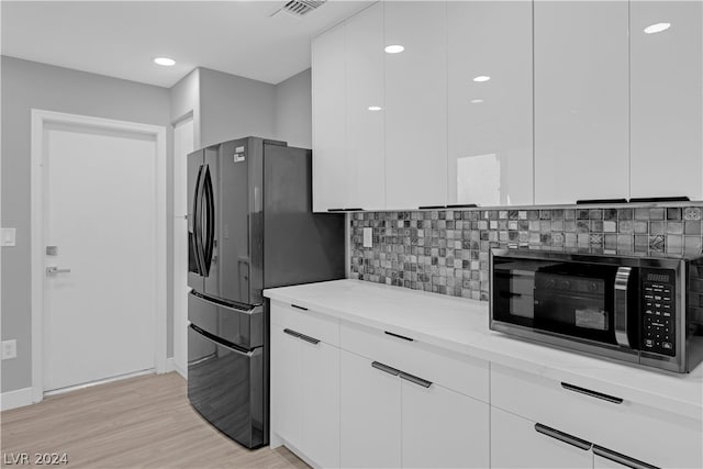 kitchen featuring backsplash, light stone countertops, light wood-type flooring, and white cabinetry