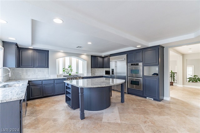 kitchen featuring light stone countertops, stainless steel appliances, a center island, and decorative backsplash