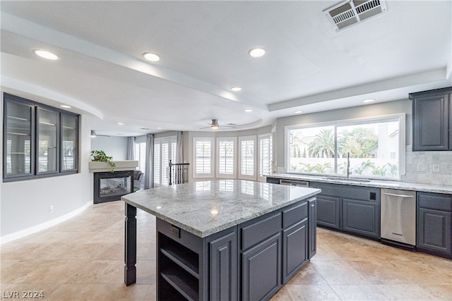 kitchen with dishwasher, light stone counters, a kitchen island, sink, and ceiling fan