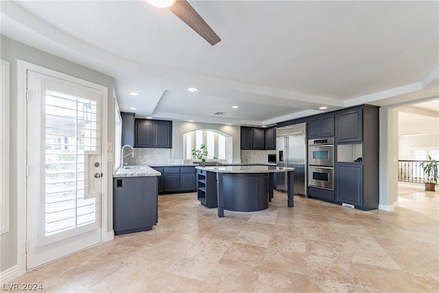 kitchen with backsplash, stainless steel appliances, a kitchen breakfast bar, a kitchen island, and light stone countertops