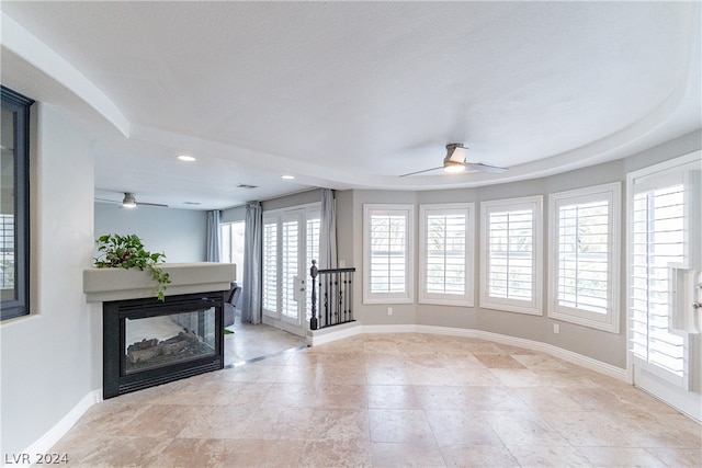 unfurnished living room with ceiling fan, a multi sided fireplace, and a textured ceiling