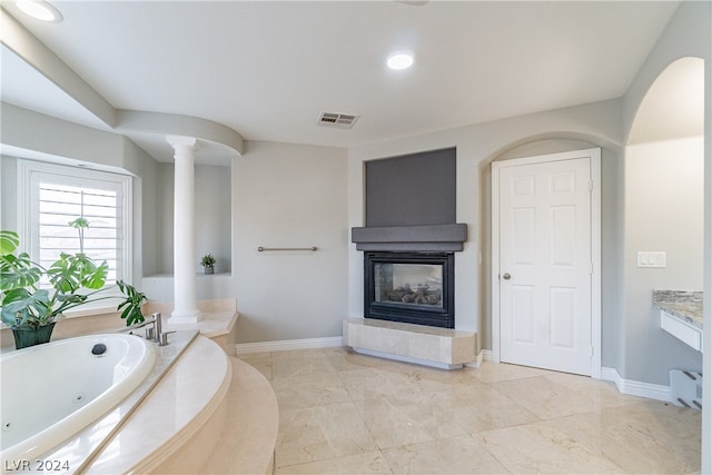 bathroom with tiled tub, vanity, a multi sided fireplace, and ornate columns