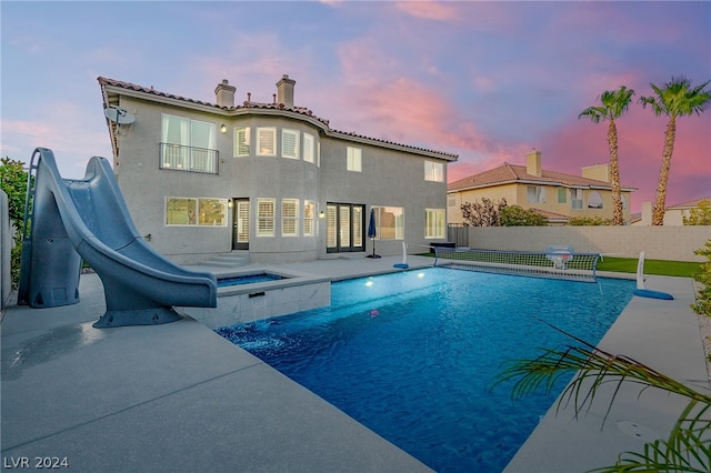 pool at dusk featuring a water slide and a patio area