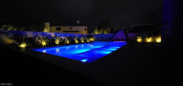 pool at night featuring a hot tub