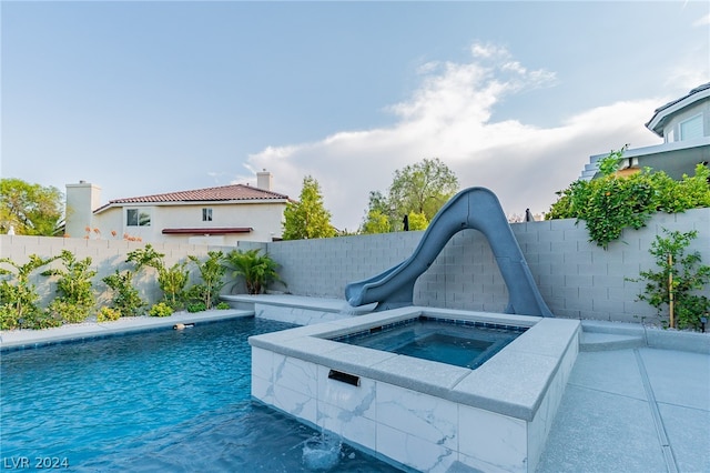 view of swimming pool featuring a water slide and an in ground hot tub