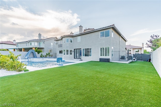 rear view of property with a fenced in pool, a lawn, and a patio