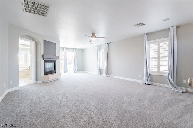 unfurnished living room featuring light colored carpet, ceiling fan, and a multi sided fireplace