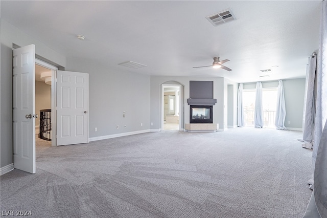 unfurnished living room with ceiling fan, a multi sided fireplace, and light carpet