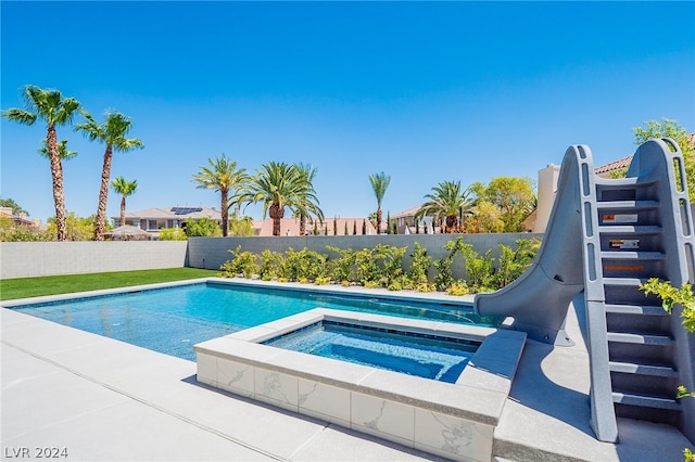 view of swimming pool featuring a water slide and an in ground hot tub