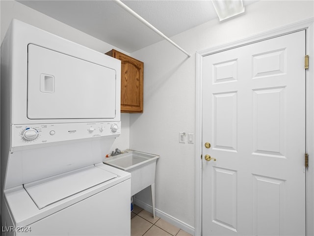 laundry room featuring cabinets, light tile patterned floors, and stacked washer and clothes dryer