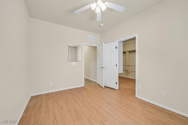 unfurnished bedroom featuring light wood-type flooring, ceiling fan, a walk in closet, and a closet