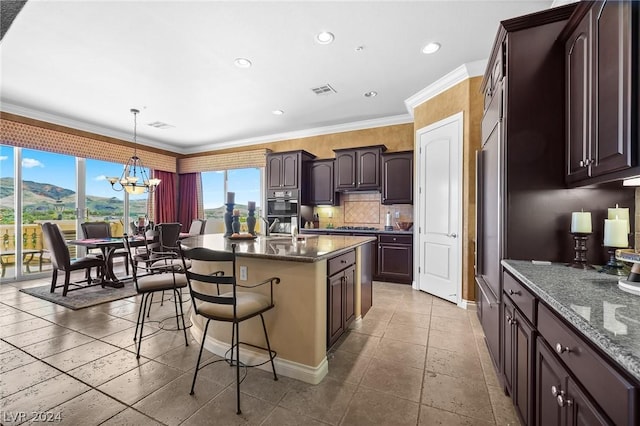 kitchen featuring an island with sink, pendant lighting, a chandelier, and dark stone counters