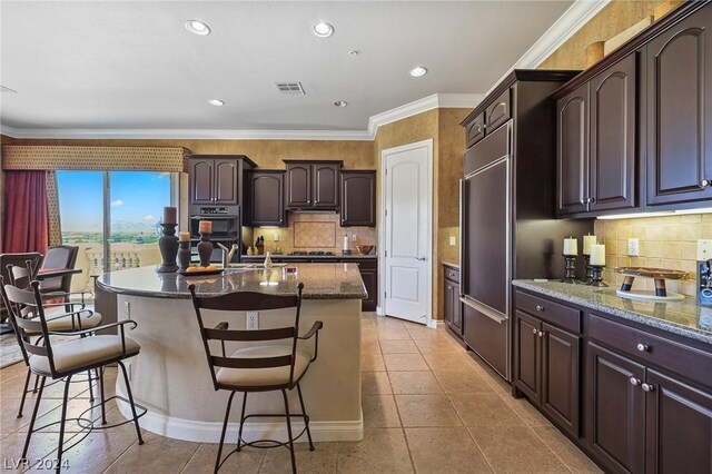 kitchen with a kitchen island with sink, ornamental molding, backsplash, and a breakfast bar