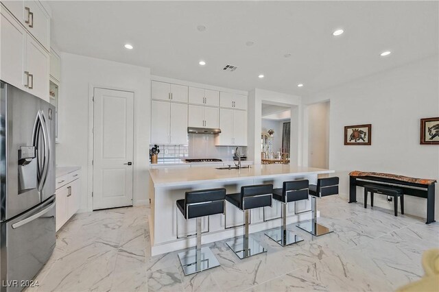 kitchen featuring a kitchen island with sink, sink, white cabinetry, and stainless steel fridge