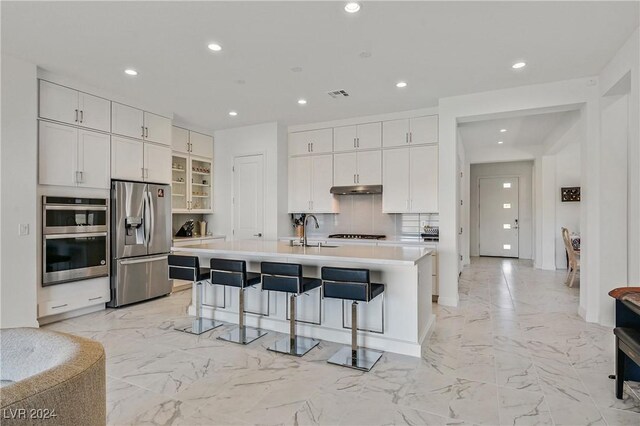 kitchen with stainless steel appliances, sink, a kitchen island with sink, white cabinets, and a kitchen breakfast bar