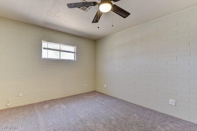 empty room with carpet floors, brick wall, and a ceiling fan