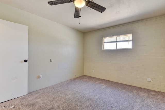 carpeted empty room with ceiling fan and brick wall