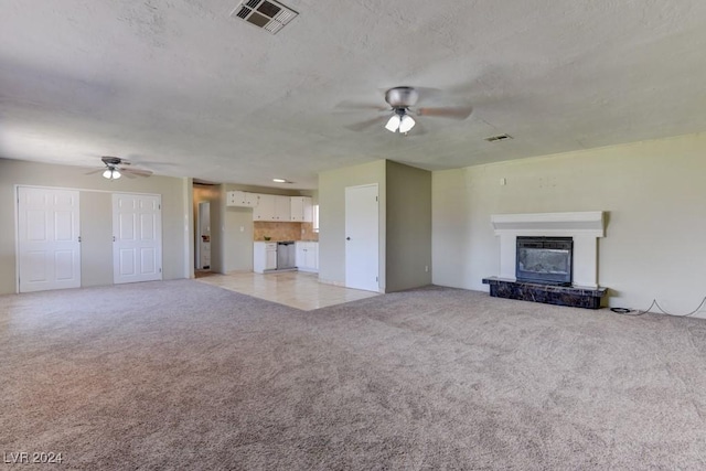 unfurnished living room featuring light colored carpet, visible vents, a ceiling fan, a glass covered fireplace, and a textured ceiling